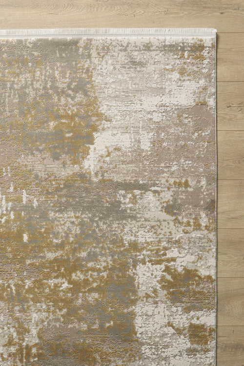 Load image 1 in gallery view. The Abstracta Gold Premium Rug - 1004G, a modern machine-made piece in beige, gold, cream, and gray with a textured, distressed abstract pattern and uneven color patches, is shown on a light wooden floor.