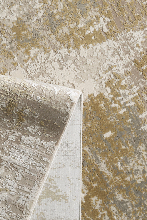 Load image 1 in gallery view. A close-up of the Abstracta Gold Premium Rug - 1004G displays its beige, gold, and taupe abstract patterns with a folded corner highlighting the machine-made texture and underside.
