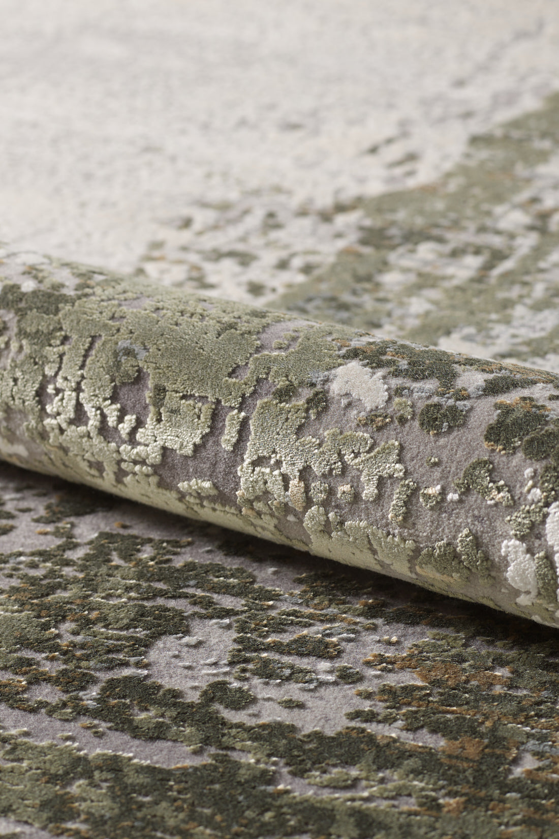 Close-up of the Abstracta Green Premium Rug - 1004H, machine-made and rolled up to showcase its textured pattern in green, gray, and cream tones, evoking a natural or abstract landscape.