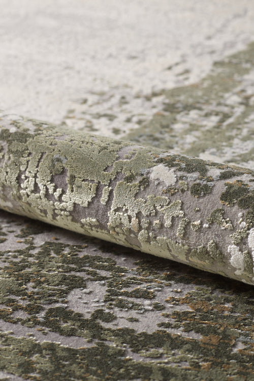 Load image 1 in gallery view. Close-up of the Abstracta Green Premium Rug - 1004H, machine-made and rolled up to showcase its textured pattern in green, gray, and cream tones, evoking a natural or abstract landscape.