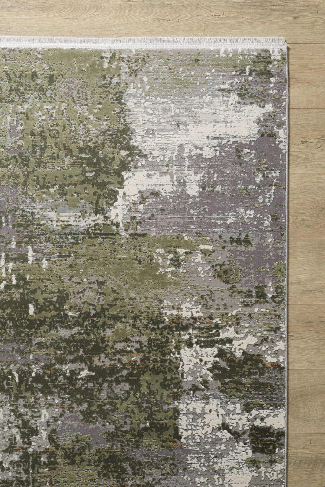 The Abstracta Green Premium Rug - 1004H, featuring an abstract design in green, gray, and white tones, adds a modern textured look to the light wooden floor with its artistic blend of colors.