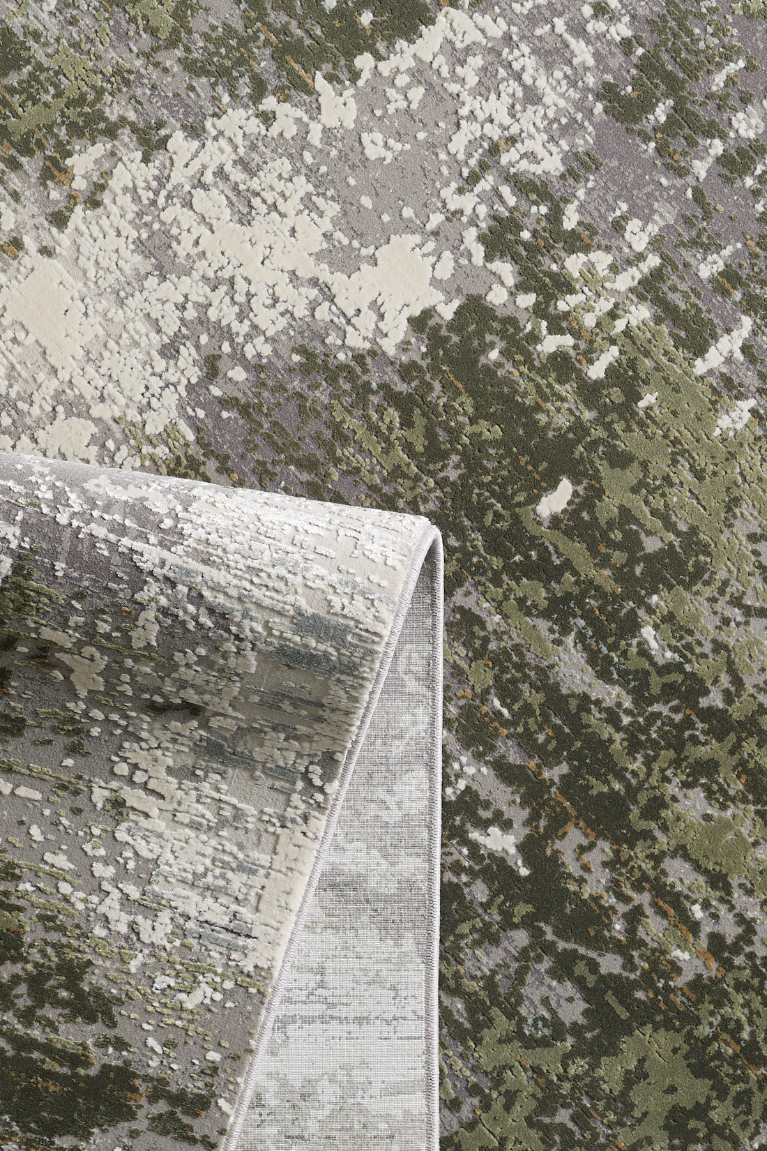 A close-up of the Abstracta Green Premium Rug - 1004H shows its abstract mottled green, gray, and cream pattern; one corner is folded to display the reverse side.