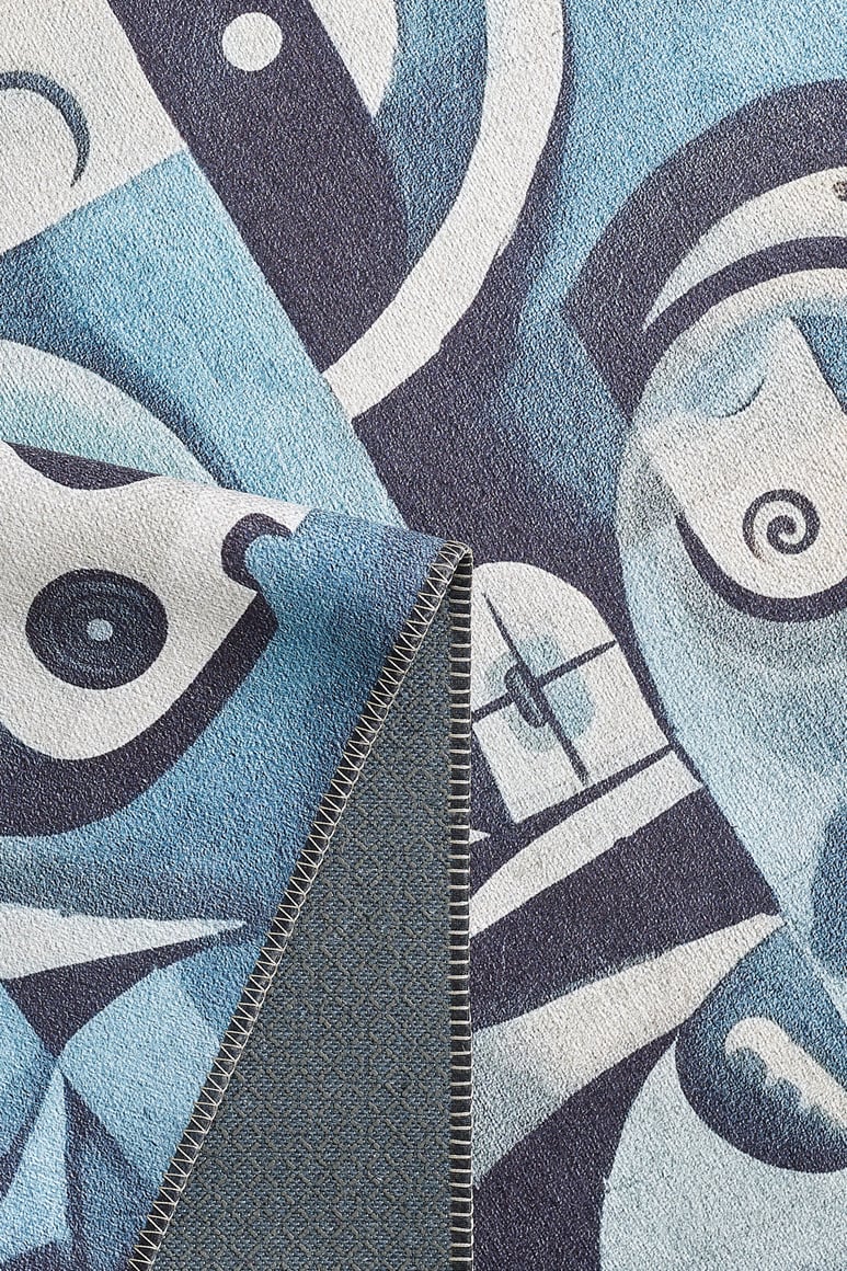 A close-up of the Aesthetic Anomaly Contemporary Washable Rug - MDJ004, showcasing its blue and white abstract geometric face pattern and stitched edge with a folded corner revealing the textured underside—ideal for high-traffic areas.