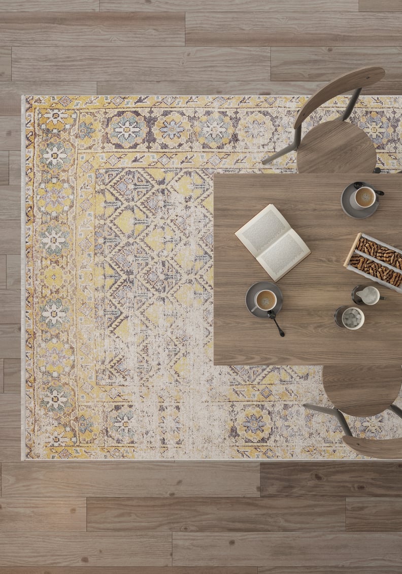 A top-down view of a wooden table with two chairs, an open book, coffee cups, and snacks set on the Aged Splendor - Washable Rug - JR1906 in yellow-gold, perfect for high-traffic areas over wood flooring.