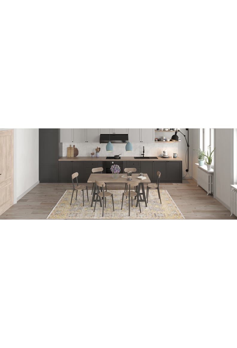 A modern dining room with a round wooden table, seven chairs, and the Aged Splendor - Washable Rug - JR1906—perfect for busy spaces. The kitchen has dark lower cabinets, white uppers, and two blue pendant lights in the background.
