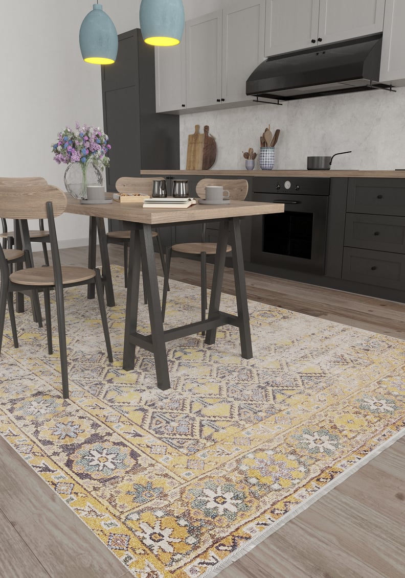 Modern kitchen with a light wood dining set atop the Aged Splendor washable rug (JR1906), great for high-traffic areas. Grey cabinets, black appliances, and blue pendants create contrast; a vase of purple flowers brightens the table.