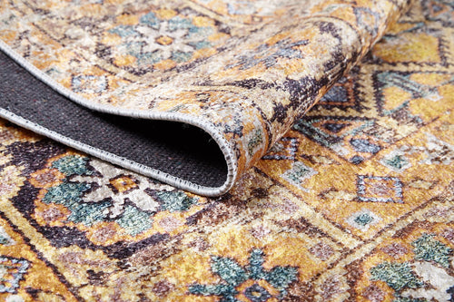 Load image 1 in gallery view. A close-up of the Aged Splendor - Washable Rug - JR1906 (Custom Size) in yellow-gold, brown, and blue earthy tones, with a folded edge revealing its dark underside and fine stitching—ideal for high-traffic areas.