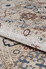 A close-up of the Aged Treasures Premium Rug - 2181A, a beige machine-made carpet featuring intricate multicolored geometric and floral patterns in blue, red, and brown. The rug is partially rolled to showcase its texture and detailed design.