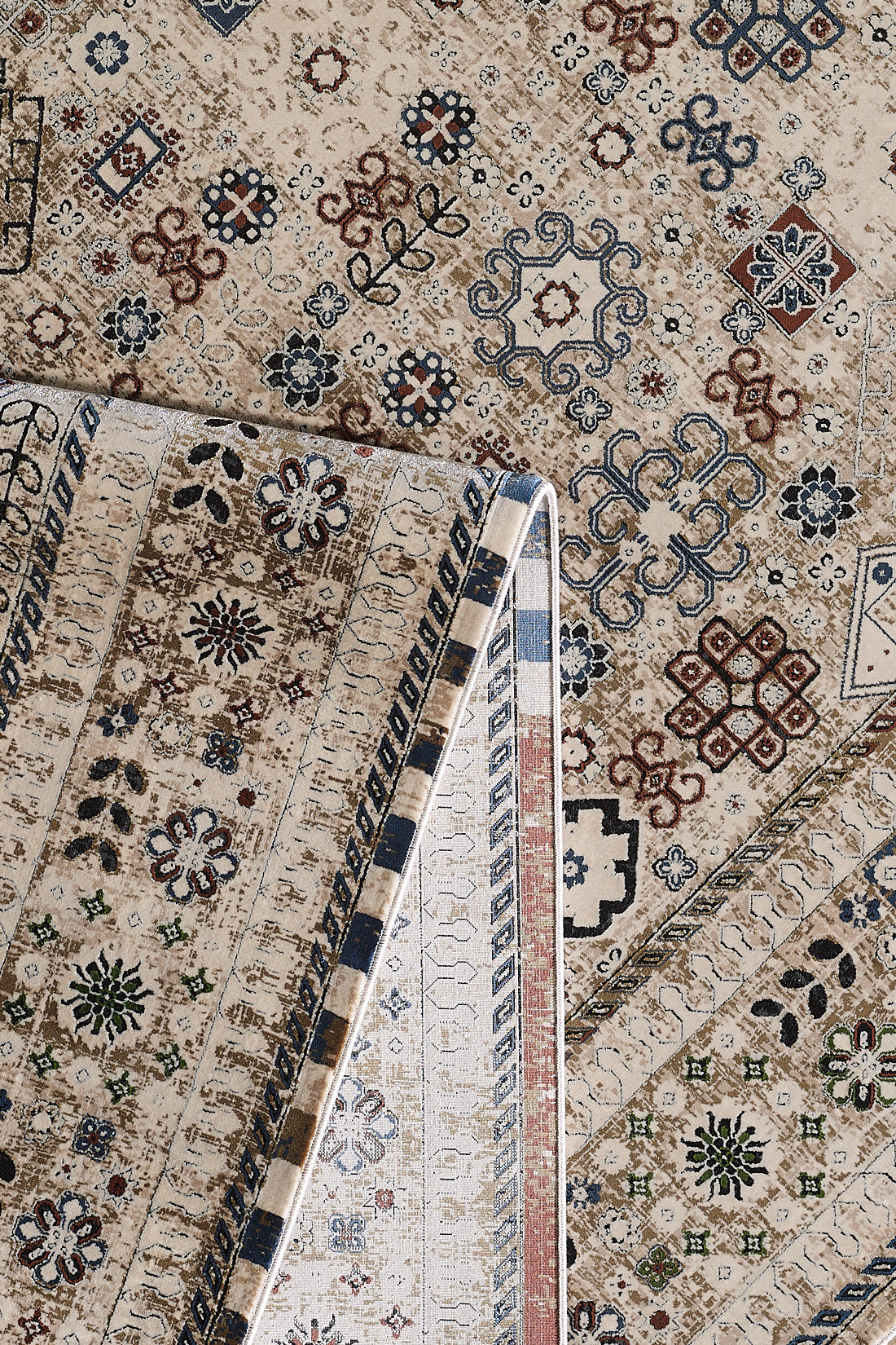 A close-up of the Aged Treasures Premium Rug - 2181A displays geometric floral motifs in beige, brown, blue, and red. One corner is folded, highlighting the machine-made underside and detailed edging.