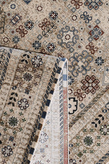 A close-up of the Aged Treasures Premium Rug - 2181A displays geometric floral motifs in beige, brown, blue, and red. One corner is folded, highlighting the machine-made underside and detailed edging.
