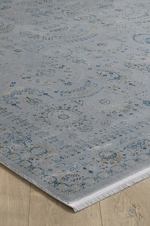 Load image 1 in gallery view. The Ancestral Motifs Turkish Rug - 2225C is a light blue, machine-made modal silk-polyester rug with intricate, faded traditional patterns in blue and beige and a fringed edge, shown atop a light wood floor.