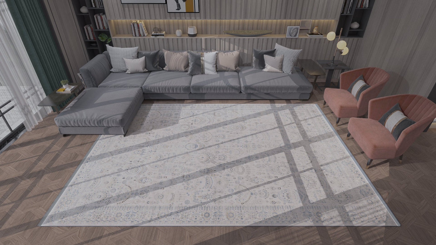 A modern living room features a large gray sectional, four striped pillows, two coral armchairs, and the Ancestral Motifs Turkish Rug - 2225C in modal silk-polyester on wooden floors. Sunlight streams through large windows across the rug.