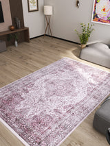 A modern living room with light wood flooring is anchored by the Ancient Emblem - Washable Rug - JR200 in pink and white, perfect for high-traffic areas. Minimalist furniture, framed art, a floor lamp, and a corner plant complete the look.
