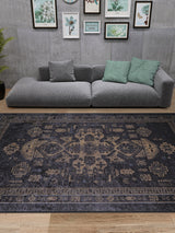 A modern living room with a gray sectional, green and gray cushions, potted plant, art on a concrete wall, and the Ancient Legacy - Washable Rug - JR1890—a large black rug ideal for high-traffic areas.