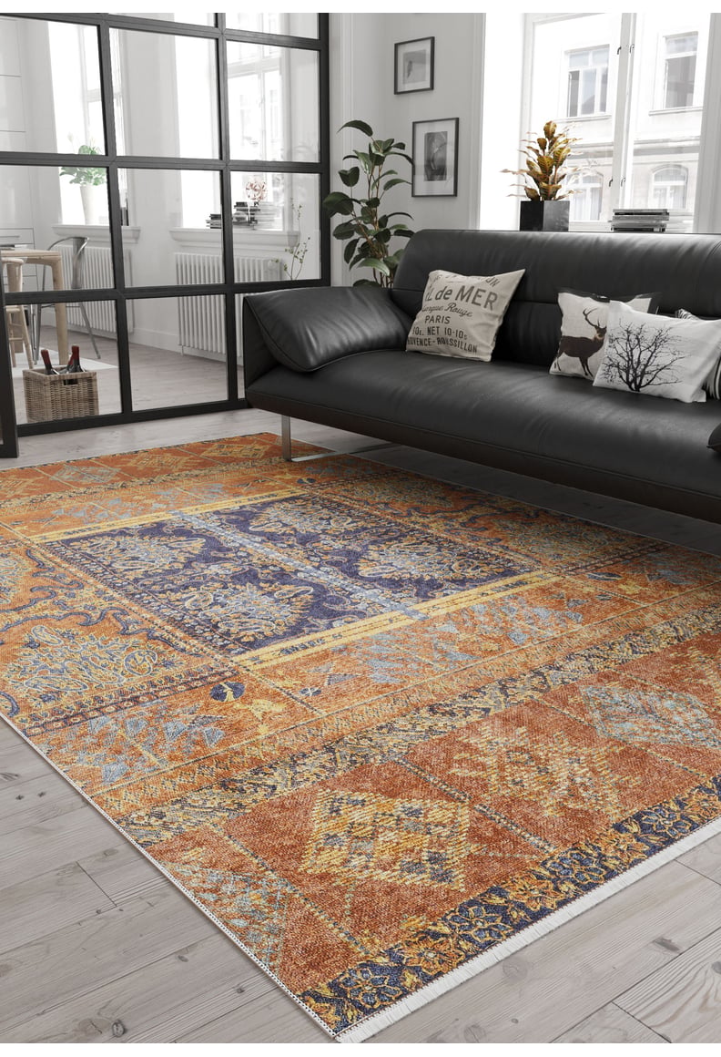 A modern living room with a dark sofa, decorative pillows, the Ancient Palace - Washable Rug - JR1864 (Custom Size) ideal for high-traffic areas, light wood flooring, a plant, and large windows streaming in natural light.