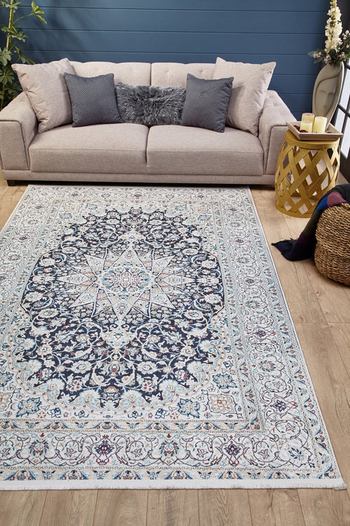 Load image 1 in gallery view. A living room with a beige sofa, gray furry pillows, and the Antique Enchantment - Washable Rug - JR1686 (Custom Size) in blue and white on wooden floors. A round yellow side table with candles and a woven basket holding a blanket sit beside the sofa.