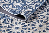 A close-up of the Antique Flourish - Washable Rug - JR1591 shows its blue base with beige floral and geometric designs. A folded corner displays the durable, washable fabric—ideal for high-traffic areas and easy to maintain.