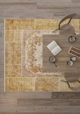 Top-down view of a wooden table with two chairs, coffee cups, an open book, and snacks atop the Antique Insignia - Washable Rug - JR309 in yellow-gold tones over a wooden floor.