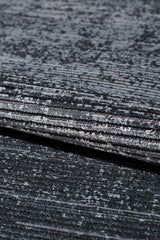 Close-up of the Antrachite Shadows Black Rug - M497A, a machine-made rug featuring textured gray and black horizontal stripes with a subtle gradient and velvety sheen. The folded view highlights its layered depth and varied shades.
