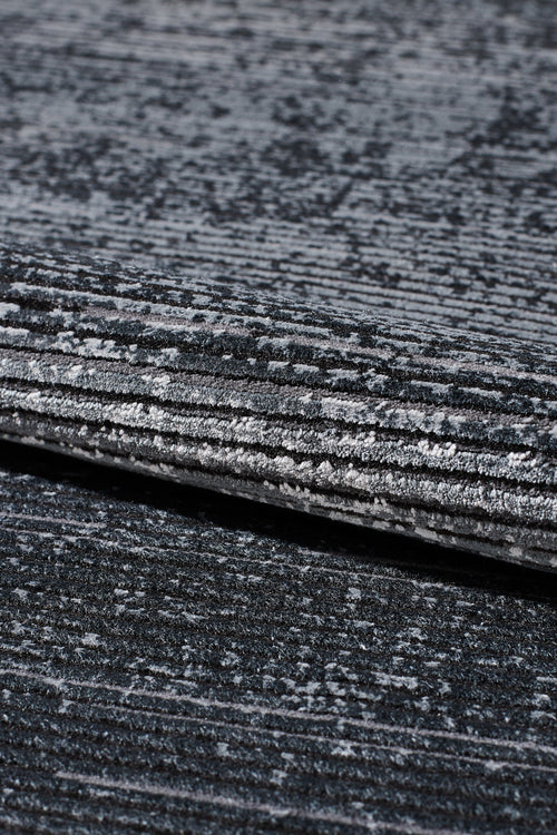 Load image 1 in gallery view. Close-up of the Antrachite Shadows Black Rug - M497A, a machine-made rug featuring textured gray and black horizontal stripes with a subtle gradient and velvety sheen. The folded view highlights its layered depth and varied shades.