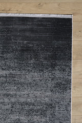 The Antrachite Shadows Black Rug - M497A features a modern gradient from dark to light gray with subtle stripes, visible fringe on the top edge, and a minimalist machine-made design—shown on a light wooden floor.
