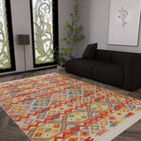 A modern living room with a dark sofa, floor lamp, leafy plant, and wooden floors features the Aqua Flow - Kilim - NMD02 rug for a pop of blue, complemented by stained glass windows with floral designs and a framed botanical print.