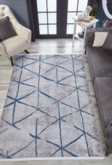 A modern living room features a beige tufted armchair, gray sofa, white side table, and the Arabesque Trellis - Washable Rug - JR1732 (Custom Size) with blue geometric lines—ideal for allergy-sensitive homes. Large glass doors complete the scene.