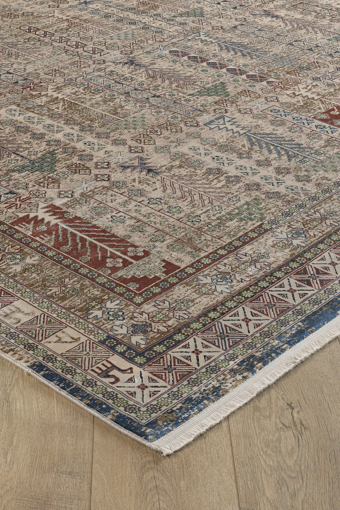 A close-up of the Archery Elegance Premium Rug - Earthy - 2183B, featuring geometric and decorative motifs in red, blue, green, and beige on a light wooden floor with fringed edges.