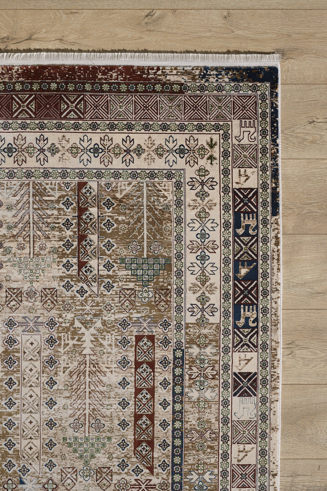 A corner of the Archery Elegance Premium Rug - Earthy - 2183B shows intricate geometric and floral patterns in brown, cream, blue, and green on a light wooden floor. This machine-made rug features a decorative border and fringed edge.