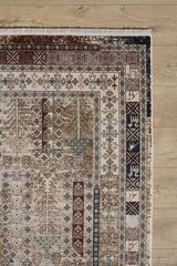 A corner of the Archery Elegance Premium Rug - Earthy - 2183B shows intricate geometric and floral patterns in brown, cream, blue, and green on a light wooden floor. This machine-made rug features a decorative border and fringed edge.