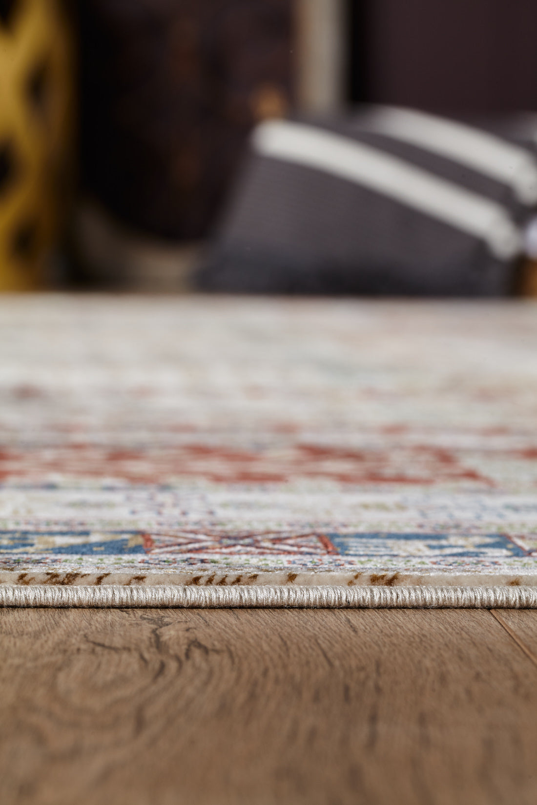 Close-up side view of the Archery Elegance Premium Rug - Earthy - 2183B, featuring a thin, colorful modern design on a wooden floor, with blurred cushions and home decor in the background.