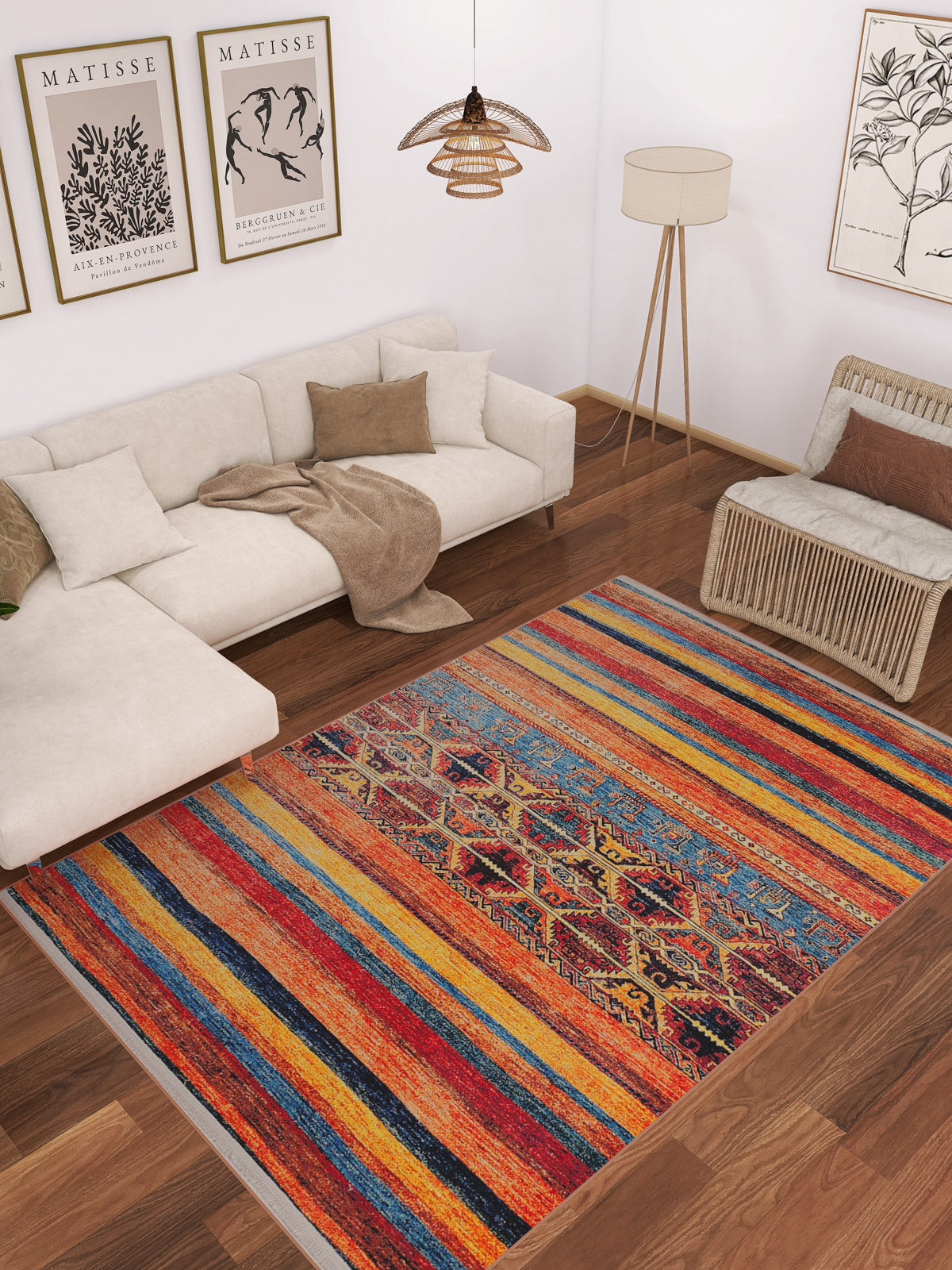 A cozy living room features a beige sectional, brown and beige pillows, a wicker chair, floor lamp, and the Arctic Chill - Washable Rug - JR860—ideal for high-traffic areas—on wood floors. Art prints decorate the white wall above the sofa.