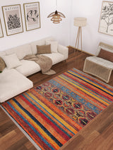 A cozy living room features a beige sectional, brown and beige pillows, a wicker chair, floor lamp, and the Arctic Chill - Washable Rug - JR860—ideal for high-traffic areas—on wood floors. Art prints decorate the white wall above the sofa.