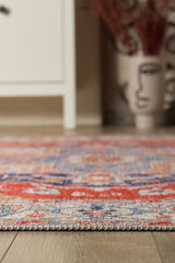 Close-up of the Ardentis Medallion Washable Rug - LCC3002 (Outlet) US in red and multicolor on a wooden floor, with a white cabinet and face-design vase blurred in the background. This washable rug adds artful style to your space.