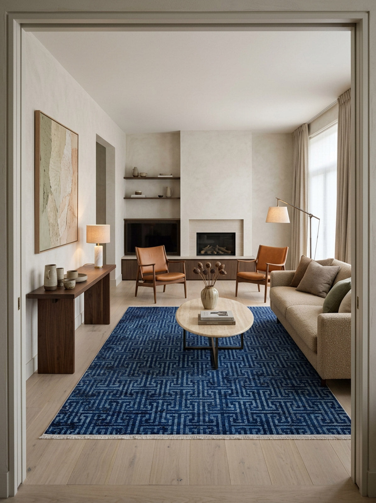 A modern living room with the Art Deco Elegance - Washable Rug - JR1224, a beige sofa, wood coffee table, brown chairs, floor lamp, fireplace, wall art, and large window with light curtains—neutral decor for a cozy feel in high-traffic spaces.