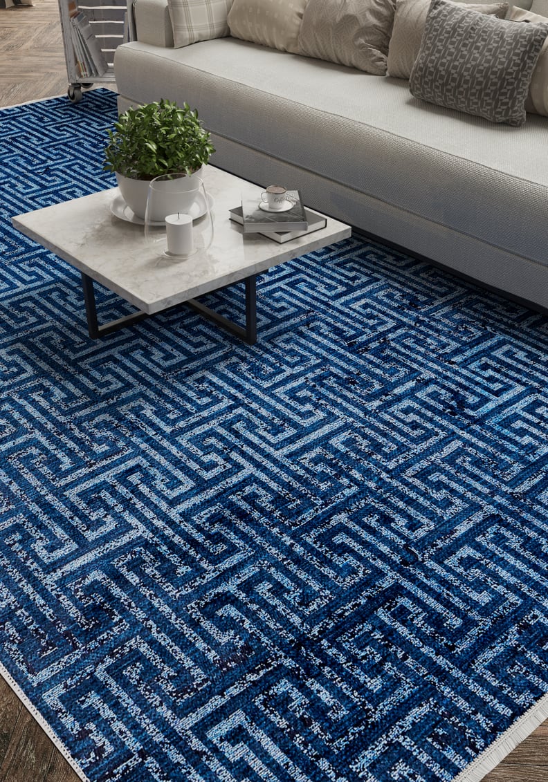 A close-up of a living room with a white sofa, gray and white pillows, a marble coffee table, and the Art Deco Elegance - Washable Rug - JR1224 in blue geometric patterns—ideal for high-traffic wooden floors.