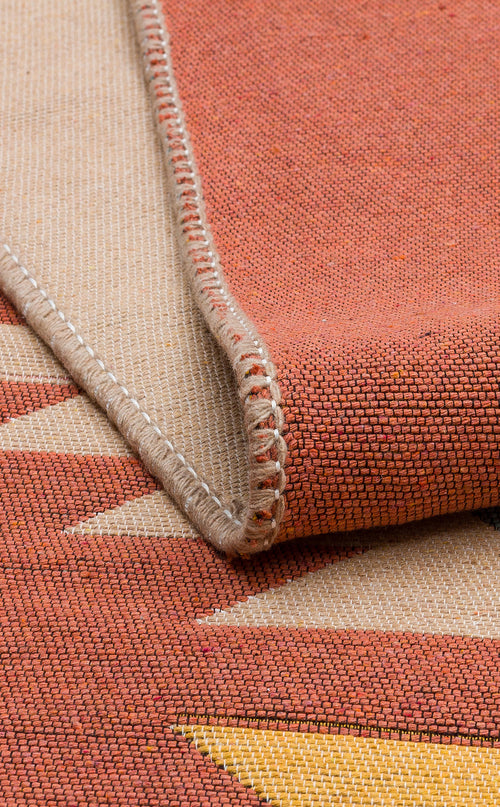Load image 1 in gallery view. Close-up of the Artisan Mesh - Washable Double-Sided Kilims - AR39, a recycled cotton rug with a red, beige, and yellow geometric pattern. The folded edge shows detailed hem stitching and highlights its textured, tightly woven surface.