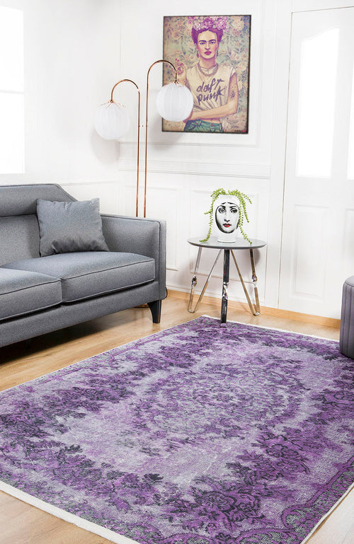 Load image 1 in gallery view. A modern living room with a gray sofa, an Artisan Tapestry - Washable Rug - JR176 (Custom Size) in purple for high-traffic areas, a round side table with a face vase, two floor lamps, and a colorful framed portrait on the wall.