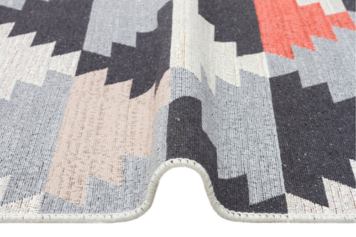 Load image 1 in gallery view. A close-up of the Artisan Touch - Washable Double-Sided Kilims - AR20 rug shows its geometric zigzag pattern in black, gray, beige, and coral tones with a wave-like fold and visible edge stitching.