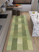 A modern kitchen with light wood floors, beige cabinets, a marble island, and the Artisanal Essence - Washable Rug - JRN32 (Custom Size) in a green patchwork checkered pattern. Fruit bowls and two wooden stools complete the look.