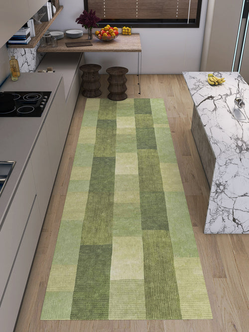 Load image 1 in gallery view. A modern kitchen with light wood floors, beige cabinets, a marble island, and the Artisanal Essence - Washable Rug - JRN32 (Custom Size) in a green patchwork checkered pattern. Fruit bowls and two wooden stools complete the look.