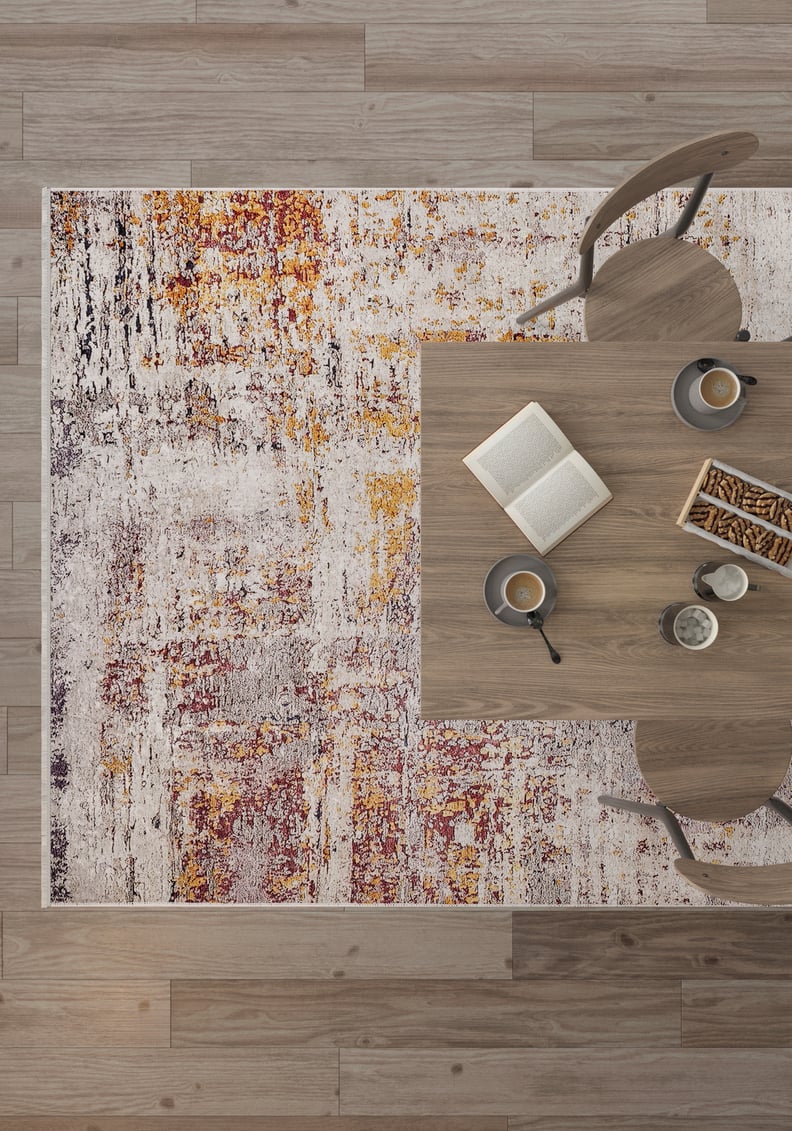A top view shows a modern table set with coffee cups, an open book, and breadsticks, surrounded by wooden chairs on the Artistic Abstraction - Washable Rug - JR775 (Custom Size) with red, orange, yellow, and white tones.