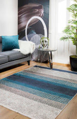 A modern living room featuring a gray sofa, teal pillow, faux fur throw, abstract wall art, side table with a plant and face-print vase, the Artistic Angles - Washable Rug - JR908 (Custom Size), and a potted palm by a white door.