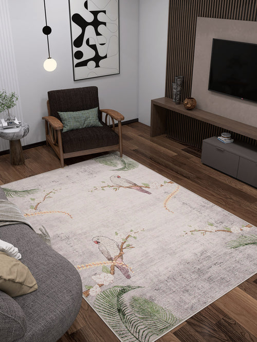 Bild 1 in Galerieansicht laden. A modern living room with dark wooden floors, a gray sofa, a wooden armchair, a wall-mounted TV, abstract wall art, and the Ashwing Silence - Washable Rug - JR0048 featuring birds and leaves.