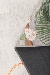 A close-up of the Ashwing Silence - Washable Rug - JR0048 shows its tropical floral pattern with green leaves and white flowers, a plain dark underside, and a subtle light-colored weave in the background.