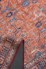 The Aurelius Coral Washable Rug - LCC3005 features a vibrant orange Persian-style flat weave with intricate blue and white patterns, shown with a folded corner revealing its detailed underside—ideal for high-traffic spaces.