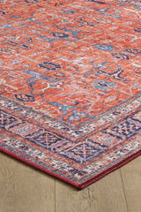 A close-up of the Aurelius Coral Washable Rug - LCC3005, featuring red flat weave with blue and white patterns and a purple border, displayed on a light wood floor—perfect for high-traffic spaces.