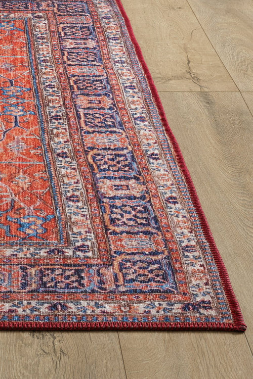 Load image 1 in gallery view. A close-up of the Aurelius Coral Washable Rug - LCC3005 shows its colorful, patterned flat weave in red, purple, and orange on a light wood floor. The detailed border and visible woven texture offer both style and durability for high-traffic areas.
