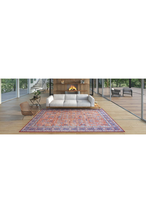 Bild 1 in Galerieansicht laden. A modern living room with large windows, a white sofa, wooden accent wall and fireplace, a washable Aurelius Coral Rug - LCC3005 (Custom Size) in pink and purple, a wicker chair, and greenery visible outside.