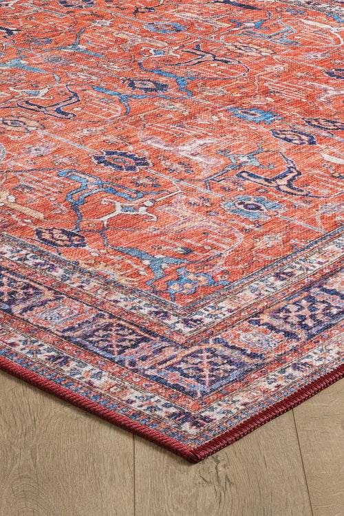 Bild 1 in Galerieansicht laden. A close-up of the Aurelius Coral Washable Rug - LCC3005 (Custom Size) on a wooden floor, showcasing its red and orange tones with blue and white accents and a purple-pink geometric border—perfect for high-traffic areas.